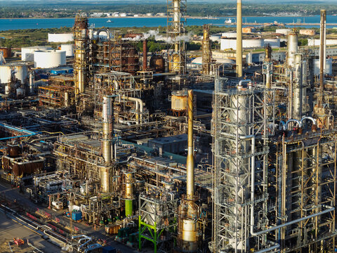 Aerial view of an oil refinery featuring complex industrial piping, tall distillation towers, and storage tanks situated near the coast in the United Kingdom.