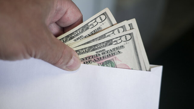 Hand Inserting Fifty Dollar Bills into White Envelope for Financial Transaction or Payment