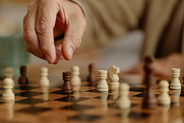 Senior playing chess moving wooden rook piece on board during leisure activity. Image useful for retirement leisure, strategic planning, intellectual wellness projects, close up © Seventyfour
