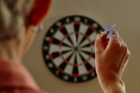 Senior woman aiming dart at board during recreational activity in senior club. Concept of precision and active retirement living for healthcare and leisure campaigns
