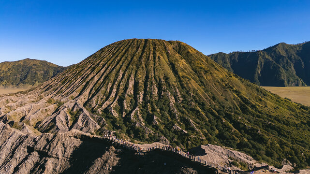 Aerial view of Mount Bromo with its distinctive volcanic crater ridges and a path filled with people walking along the rim in Tosari, East Java, Indonesia.