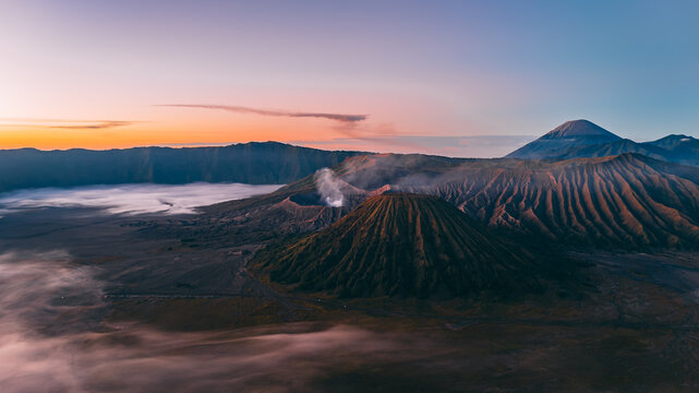 Aerial view of Mount Bromo with volcanic craters, rugged slopes, and morning mist under a soft sunrise sky in Tosari, East Java, Indonesia.
