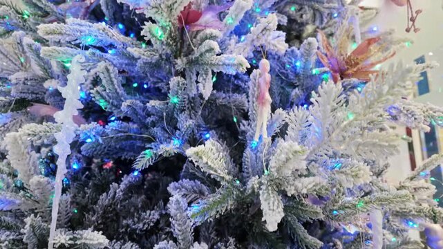 Snow flocked fir branches decorated with glowing string lights, icicle ornaments and angel figurines.