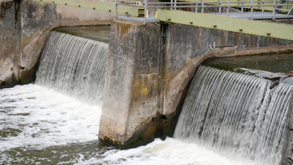 concrete river weir with fast rushing water flowing down in cascades © Flowal93