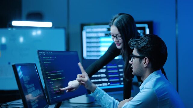 Two professional software developers collaborating in a modern tech office, pointing at computer screens with programming code, working together on a software engineering project and IT startup.