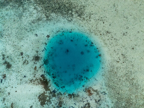 Aerial view of a vibrant blue lagoon surrounded by shallow coral reefs and clear turquoise water near Karimun Jawa island, Karimunjawa, Central Java, Indonesia.