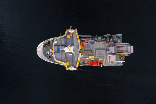 Aerial view of a salmon slaughter boat on dark water, featuring processing equipment, a small orange rescue boat, and industrial machinery in Liabygda, More og Romsdal, Norway.