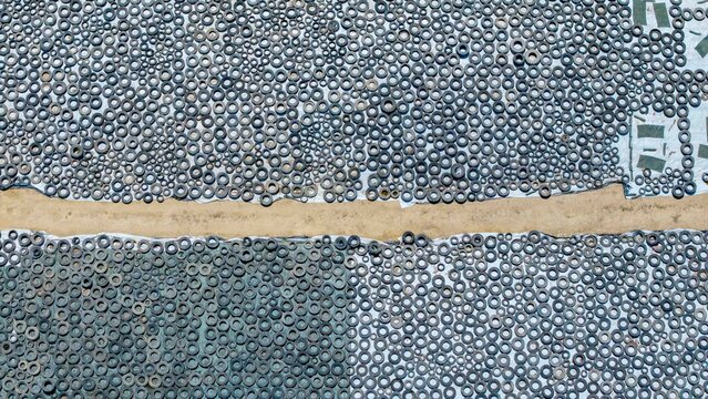 Aerial view of thousands of discarded rubber tires arranged in organized rows on the ground separated by a dirt path in Philadelphia, Western Cape, South Africa.