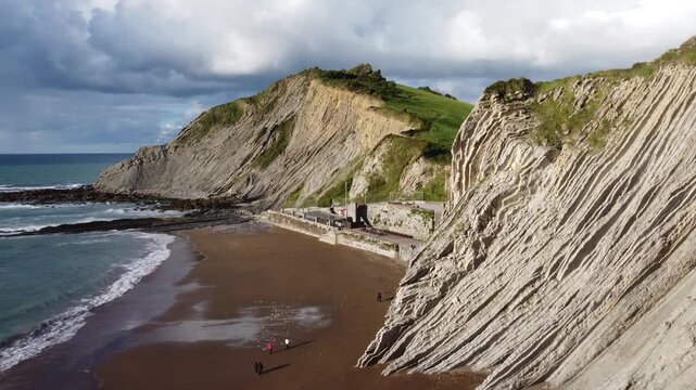 Aerial View of Flysch Cliffs and Sandy Beach with Waves at Zumaia, Basque Country, Spain.  Ideal for travel promos, geology documentaries, educational content and outdoor brand videos.