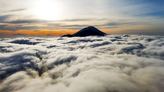 Aerial view of Mount Batur rising above a thick sea of clouds during a golden sunrise in Kintamani, Bali, Indonesia.