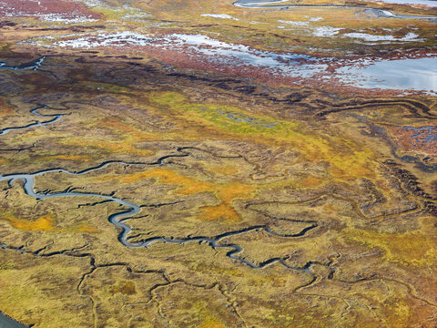 Aerial view of the winding Knik River meandering through the vast, colorful tundra landscape, showcasing intricate water channels and autumn vegetation in Knik River, Alaska, United States.