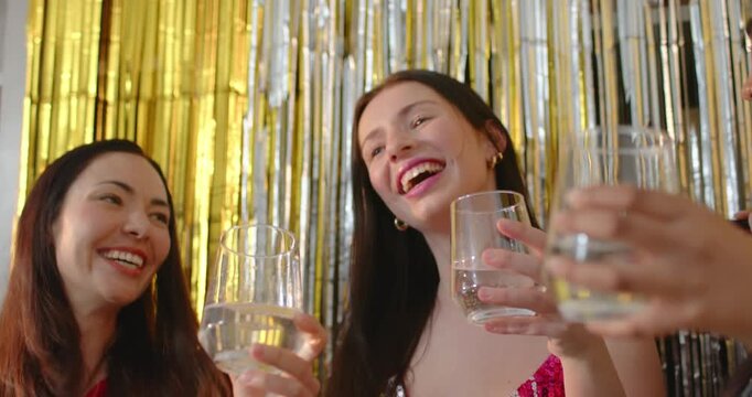 Diverse women clinking clear glasses after woman in pink sequin dress flipping hair at fringe wall