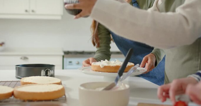 Hands reaching bowls on counter, bakers and child are assembling and decorating cake with berries