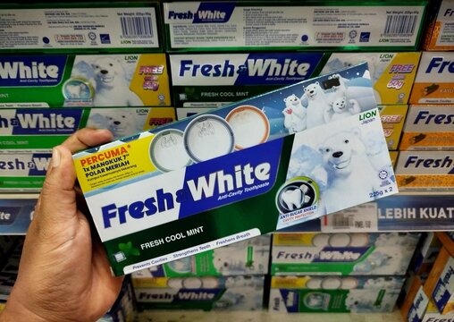 KUALA TERENGGANU MALAYSIA- OKTOBER 08. 2026: Hand holding a Fresh & White toothpaste box with polar bear design in a store aisle, surrounded by multiple variants of the same brand on shelves.