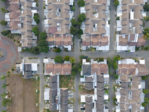 Aerial view of a dense residential neighborhood with uniform brown-roofed houses, paved streets, and scattered green trees in Indonesia.