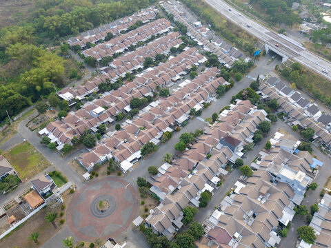 Aerial view of a residential neighborhood with rows of houses featuring brown roofs, a circular roundabout, and nearby roads in Indonesia.