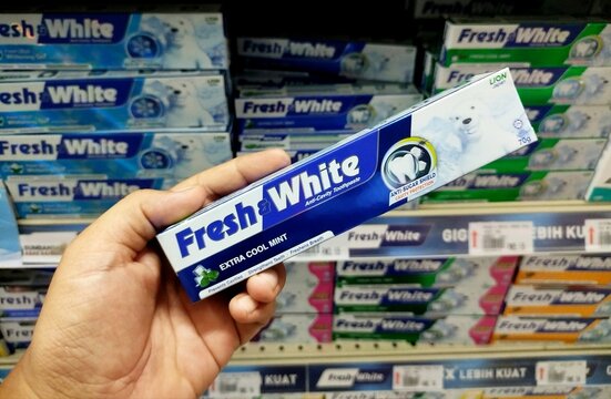 KUALA TERENGGANU MALAYSIA- OKTOBER 08. 2026: Hand holding a Fresh & White Extra Cool Mint toothpaste box in a store aisle, surrounded by multiple toothpaste packs on retail shelves.
