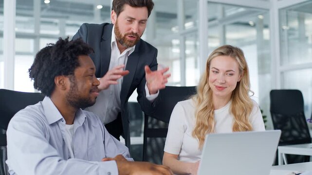 Three multiracial business team in office Caucasian leader boss talking happy satisfied with online laptop good result achieve talk to colleagues coworkers multiethnic group teamwork job with computer