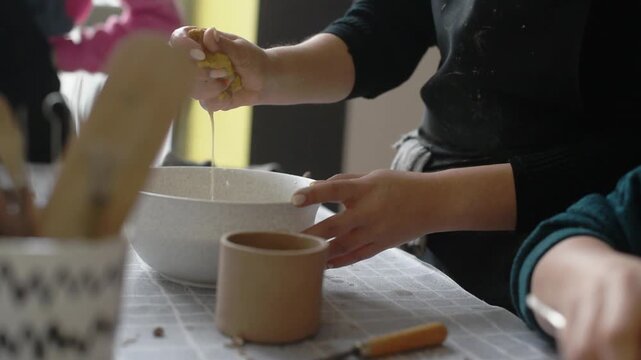 Pottery tools and ceramic workspace, hands working with wooden tool near clay bowl and cups on table. Craft hobby concept for art supplies ads, potter shapes clay piece