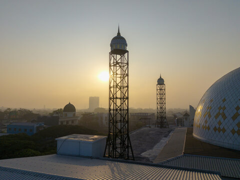 Aerial view of a mosque with metal-lattice minarets and a dome at sunset in Malang, East Java, Indonesia.