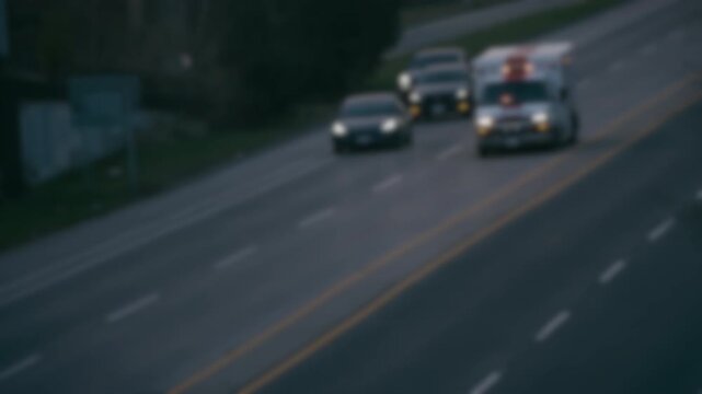 Soft focus of a white ambulance driving down a road with lights flashing. Passing cars pull over to the side to let ambulance the priority of way.
