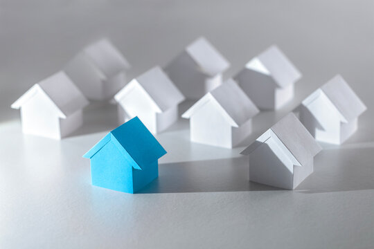 Searching for real estate property blue paper house standing out from background houses