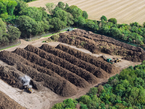 Aerial view of a biogas facility featuring large rows of organic compost piles and heavy machinery operating in a rural setting in the United Kingdom.