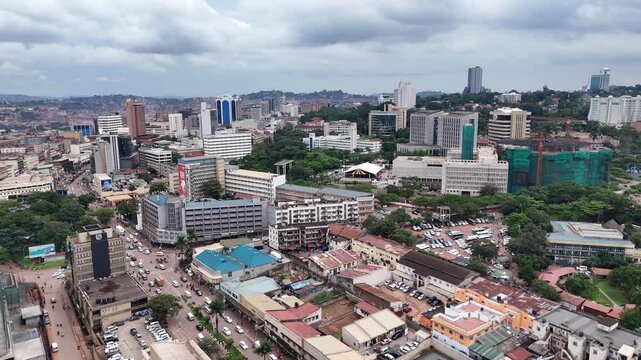 Aerial view of the bustling cityscape of Kampala with modern office buildings, dense urban infrastructure, and lush green trees under a cloudy sky in Kampala, Central Region, Uganda.