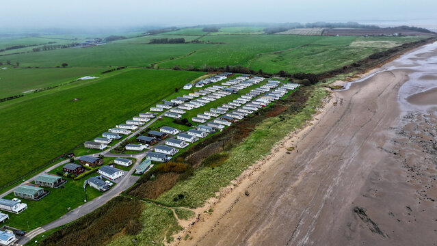 Aerial view of the Southerness caravan park with rows of static mobile homes, green fields, and a sandy beach in Southerness, Scotland, United Kingdom.