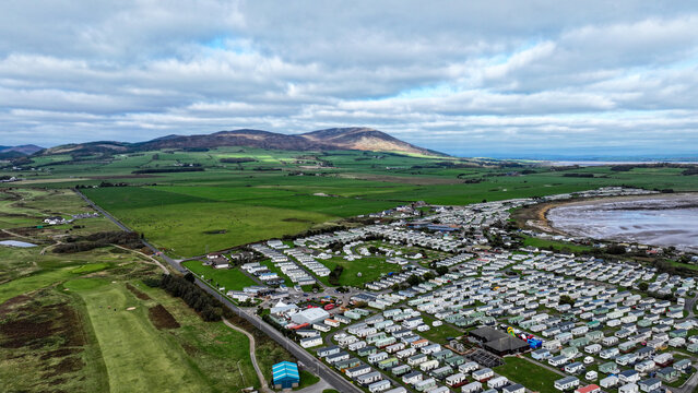 Aerial view of the Southerness holiday park with numerous static caravans, green fields, and coastal landscape under a cloudy sky in Southerness, Scotland, United Kingdom.