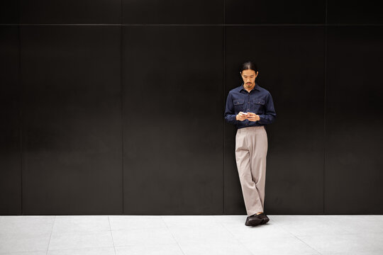 Man Standing by a Wall While Looking at His Phone