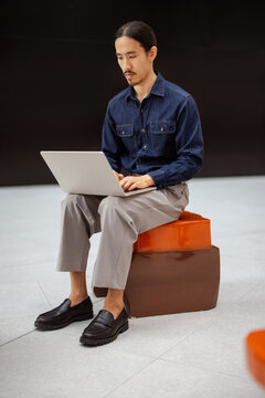 Man Working on Laptop While Sitting on a Colorful Block