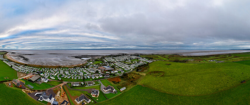 Aerial view of Southerness holiday park featuring rows of caravans, green fields, and a coastal landscape under a cloudy sky in Southerness, Scotland, United Kingdom.