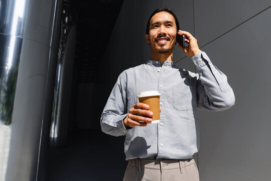 Man Talks on Phone While Holding Coffee Cup in City Street