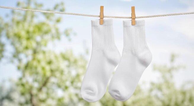 Pair of white crew socks hanging on a clothesline with wooden clothespins outdoors