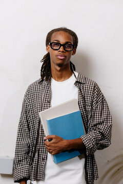 Cheerful Black entrepreneur with dreadlocks holding books and smiling.