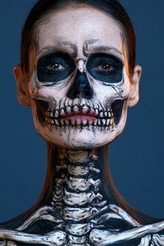 Adult with monochrome skeleton face paint and amber halo on deep blue background