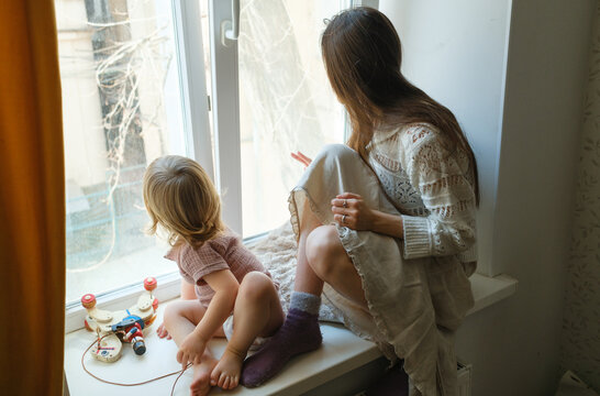 Mother and young child looking out the window while sitting on a windo