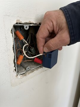 Electrician inserting neutral white wire into compact blue smart switch relay inside metal wall box