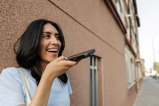 Young woman smiling while using voice command on smartphone