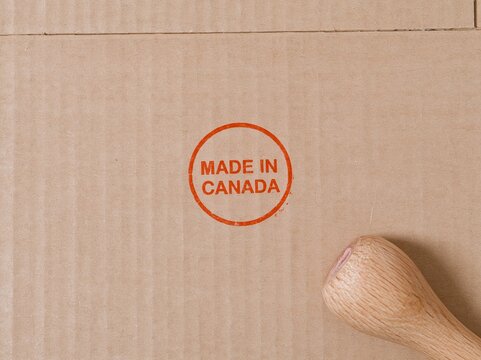 Made in Canada stamp impression on textured cardboard with a wooden handle, featuring burnt orange ink for export and product origin concepts