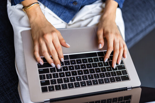 Woman Typing on a Laptop While Sitting on a Couch in a Home