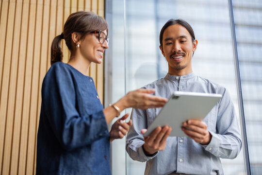 Two People Discuss Work While Standing Near a Large Window
