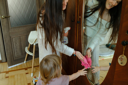 Mother and child cleaning a mirror together at home