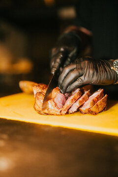 Chef slices roasted meat on a cutting board in a dark kitchen