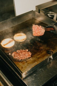 Cook places raw meat patties on a hot grill in a commercial kitchen