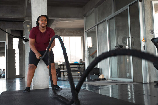 Determined African American woman performing an intense battle rope workout in a modern gym highlighting strength training endurance and an active inclusive lifestyle for commercial campaigns.