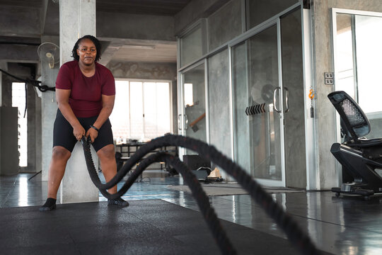 Determined African American woman performing an intense battle rope workout in a modern gym highlighting strength training endurance and an active inclusive lifestyle for commercial campaigns.
