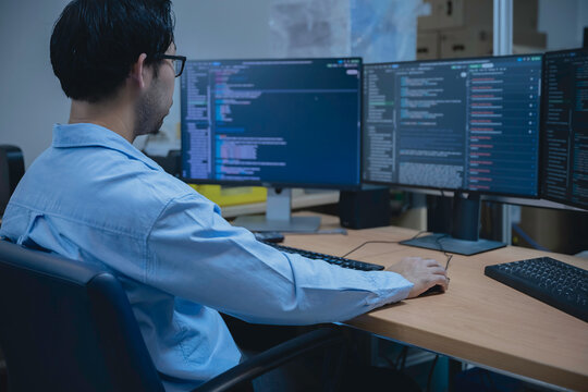 Computer programmer analyzes code across multiple screens while developing and testing software, representing coding, problem solving, productivity, and modern IT work.
