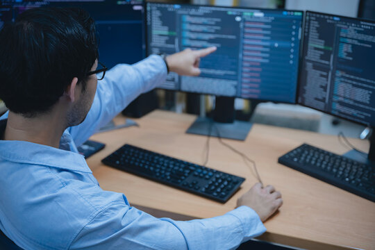 Computer programmer analyzes code across multiple screens while developing and testing software, representing coding, problem solving, productivity, and modern IT work.